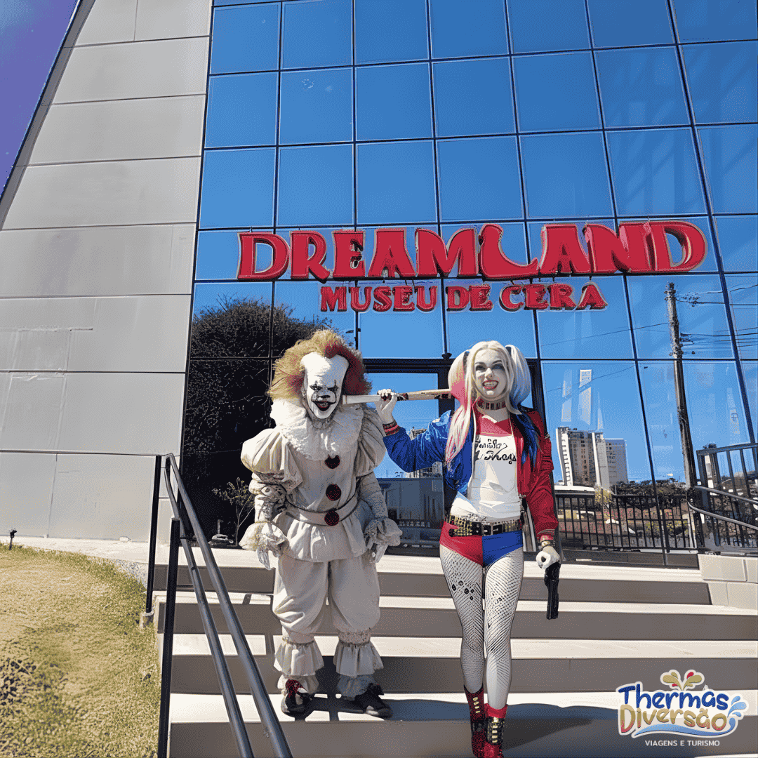 Fachada espelhada do Dreamland Museu de Cera em Olímpia, com duas figuras caracterizadas como personagens de filmes posando nas escadarias, representando a experiência única e imersiva oferecida pelo museu.