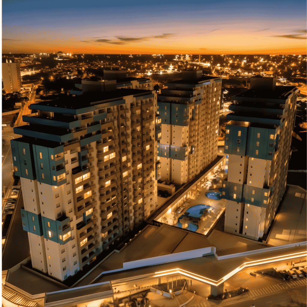 Vista aérea noturna do Enjoy Olímpia Park Resort iluminado, com suas torres modernas destacadas sob o pôr do sol e a cidade de Olímpia ao fundo, transmitindo conforto, sofisticação e clima de férias.
