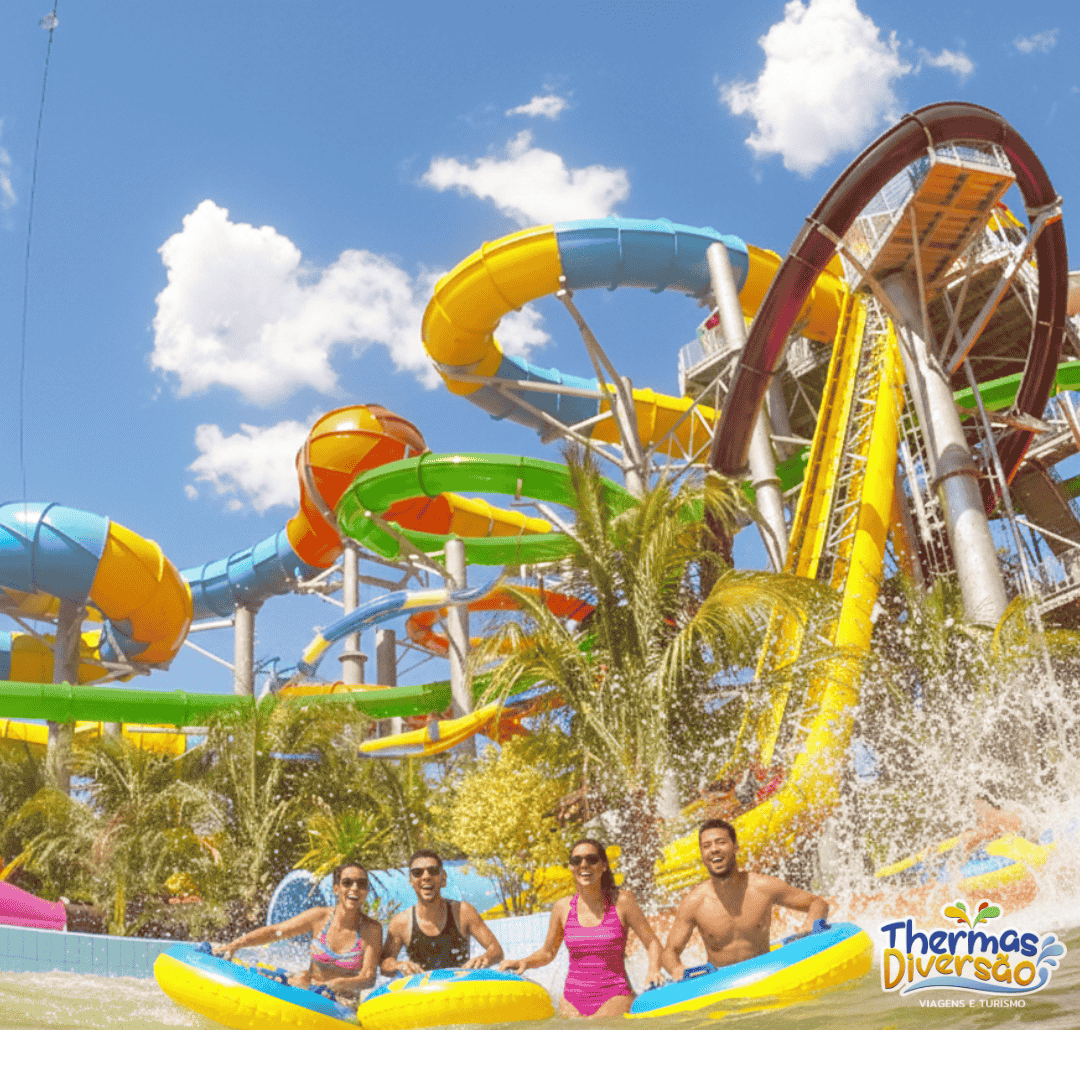 Grupo de amigos se divertindo nas boias em uma das piscinas do Thermas dos Laranjais, em Olímpia, com toboáguas coloridos e céu azul ao fundo
