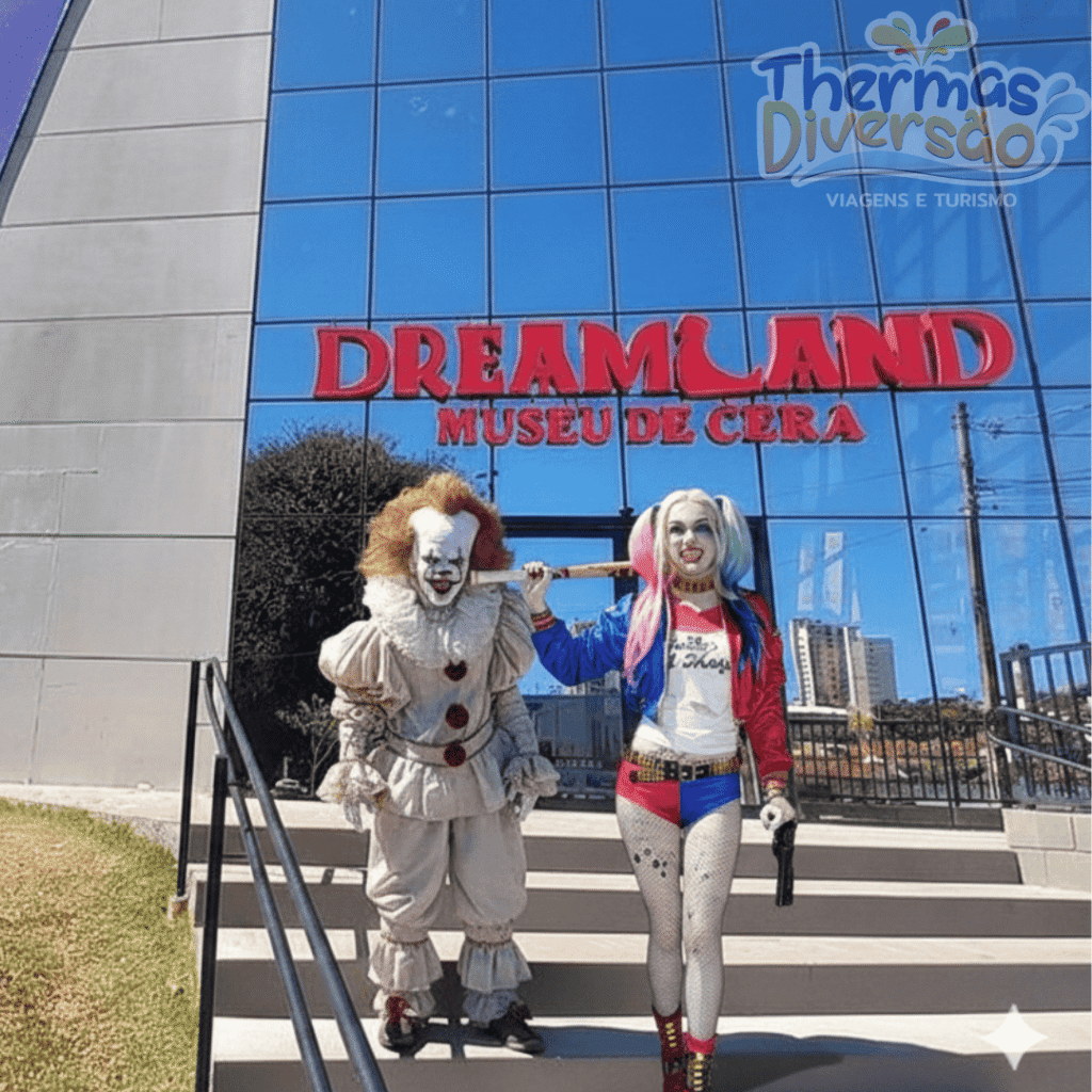 Entrada do Dreamland Museu de Cera Olímpia com personagens realistas do cinema, incluindo Pennywise e Arlequina, atraindo visitantes para fotos em frente à fachada moderna de vidro espelhado.