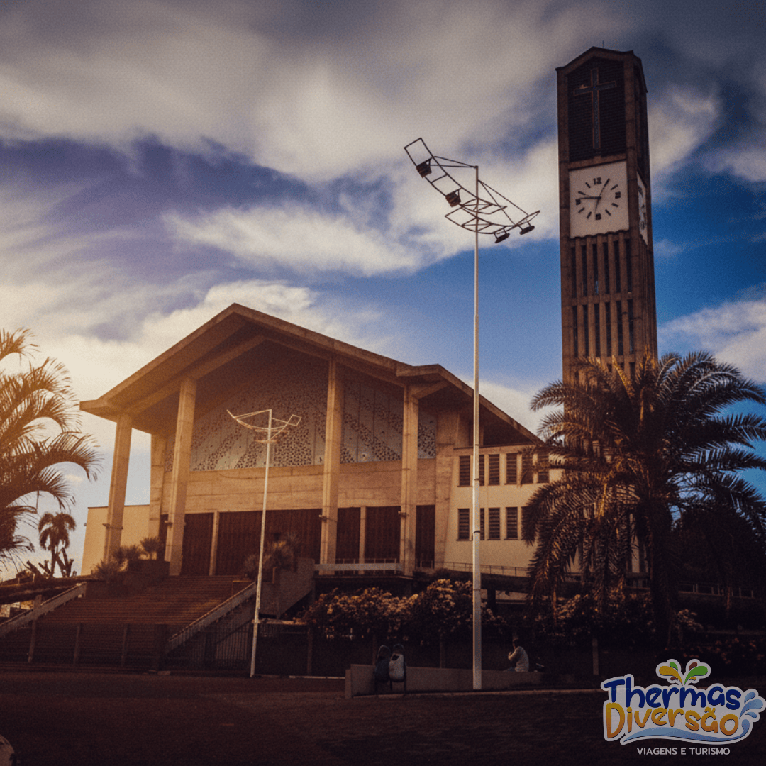 Igreja Matriz de São João Batista no entardecer, com luz suave destacando a torre do relógio e a arquitetura moderna da igreja.